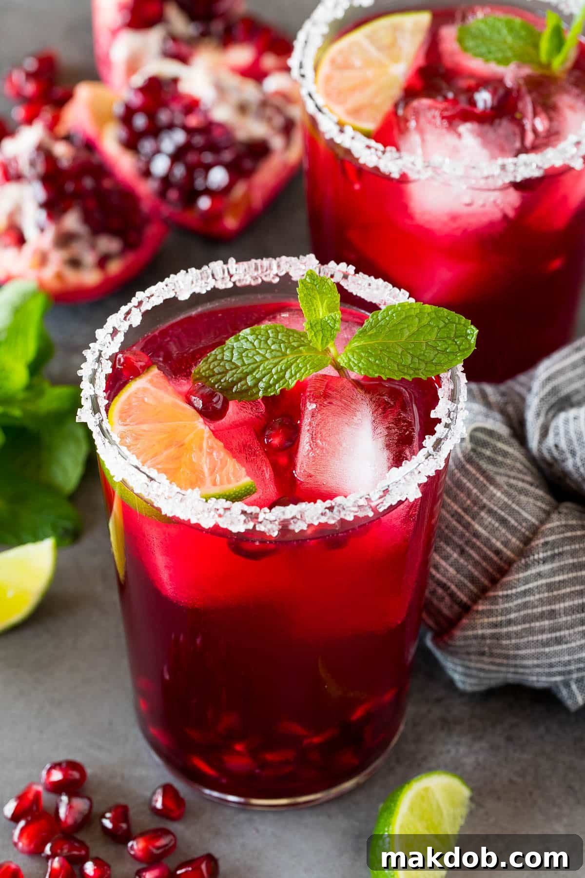 A vibrant pomegranate margarita in a sugar-rimmed glass, garnished with fresh mint and a lime slice, perfect for holiday entertaining.