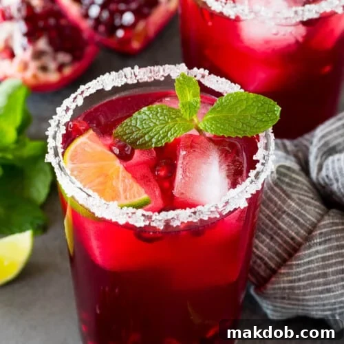 A pomegranate margarita in a sugar rimmed glass with mint and lime for garnish.