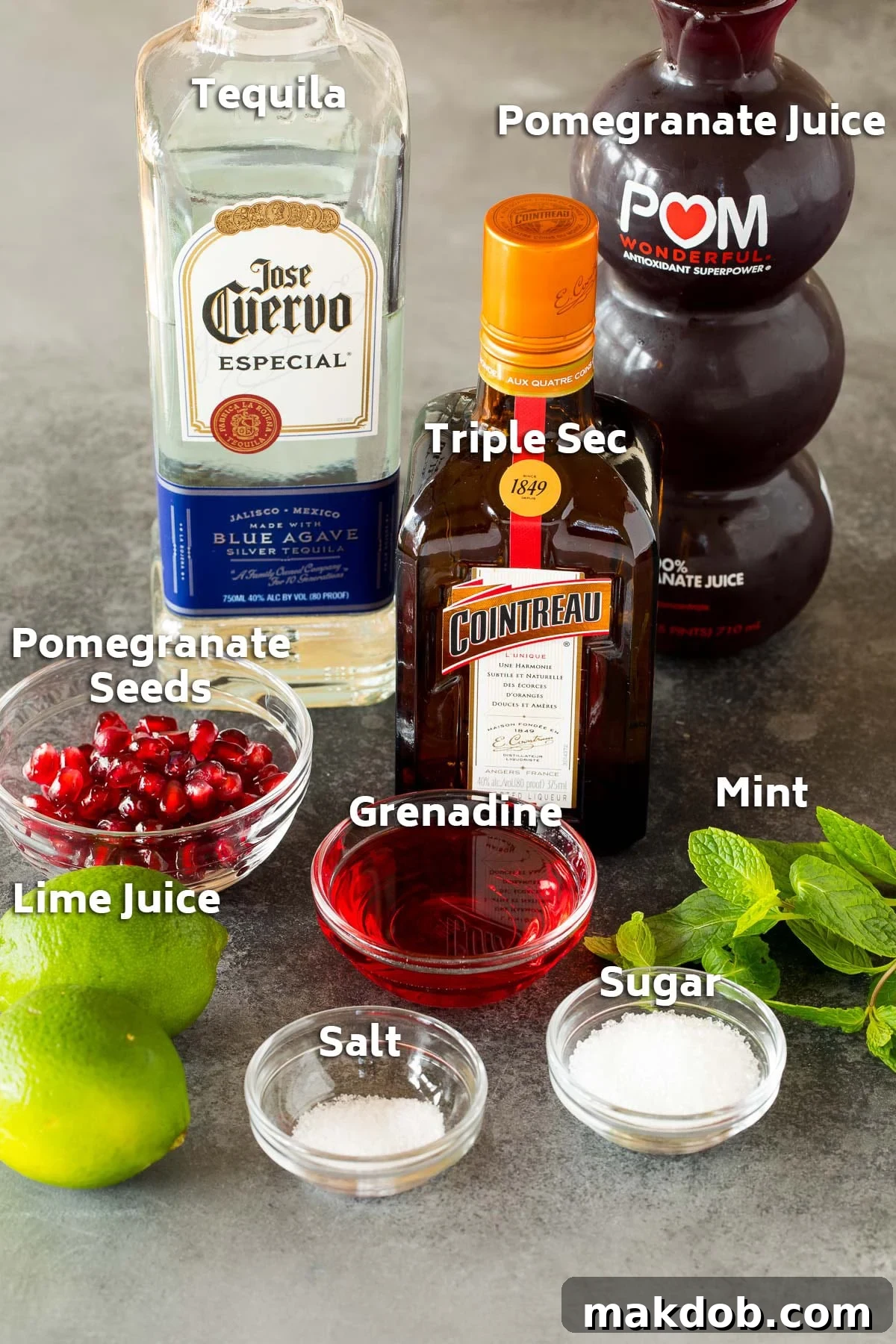 Ingredients for a pomegranate margarita: fresh juice, grenadine, tequila, sugar, and salt, artfully arranged.