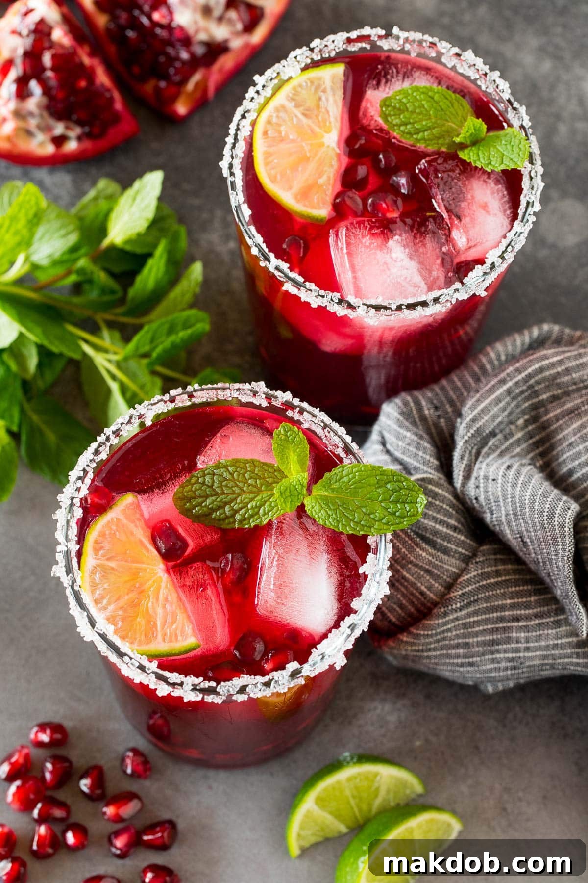 Two glasses of vibrant pomegranate margarita, garnished with lime, mint, and fresh pomegranate arils, ready for enjoyment.