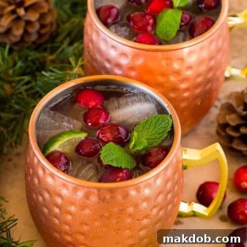 Mugs of cranberry moscow mule topped with fresh cranberries.