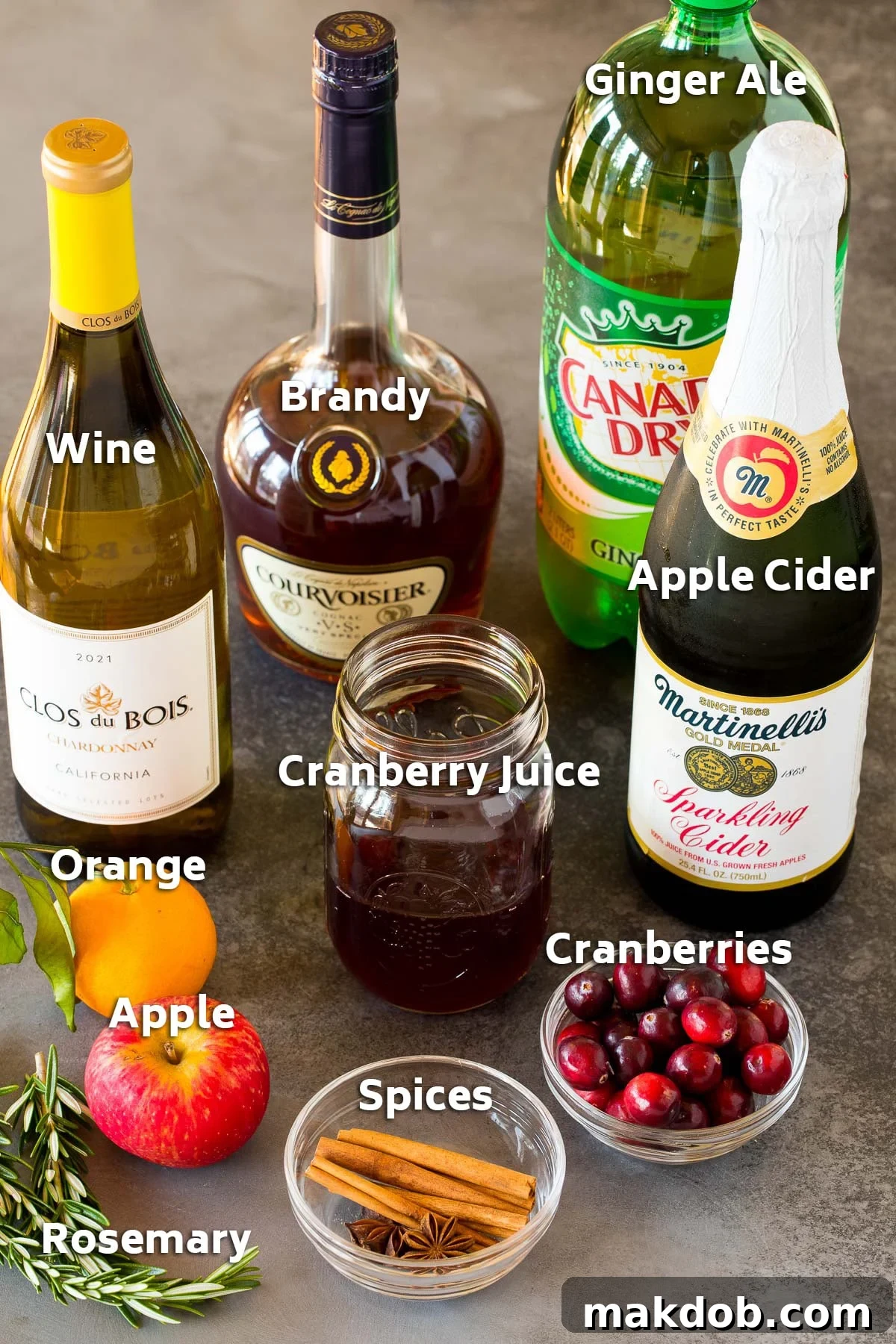 Jolly Christmas Sangria 3 Ingredients including bottles of brandy, wine, apple cider, ginger ale and also fruit and spices.