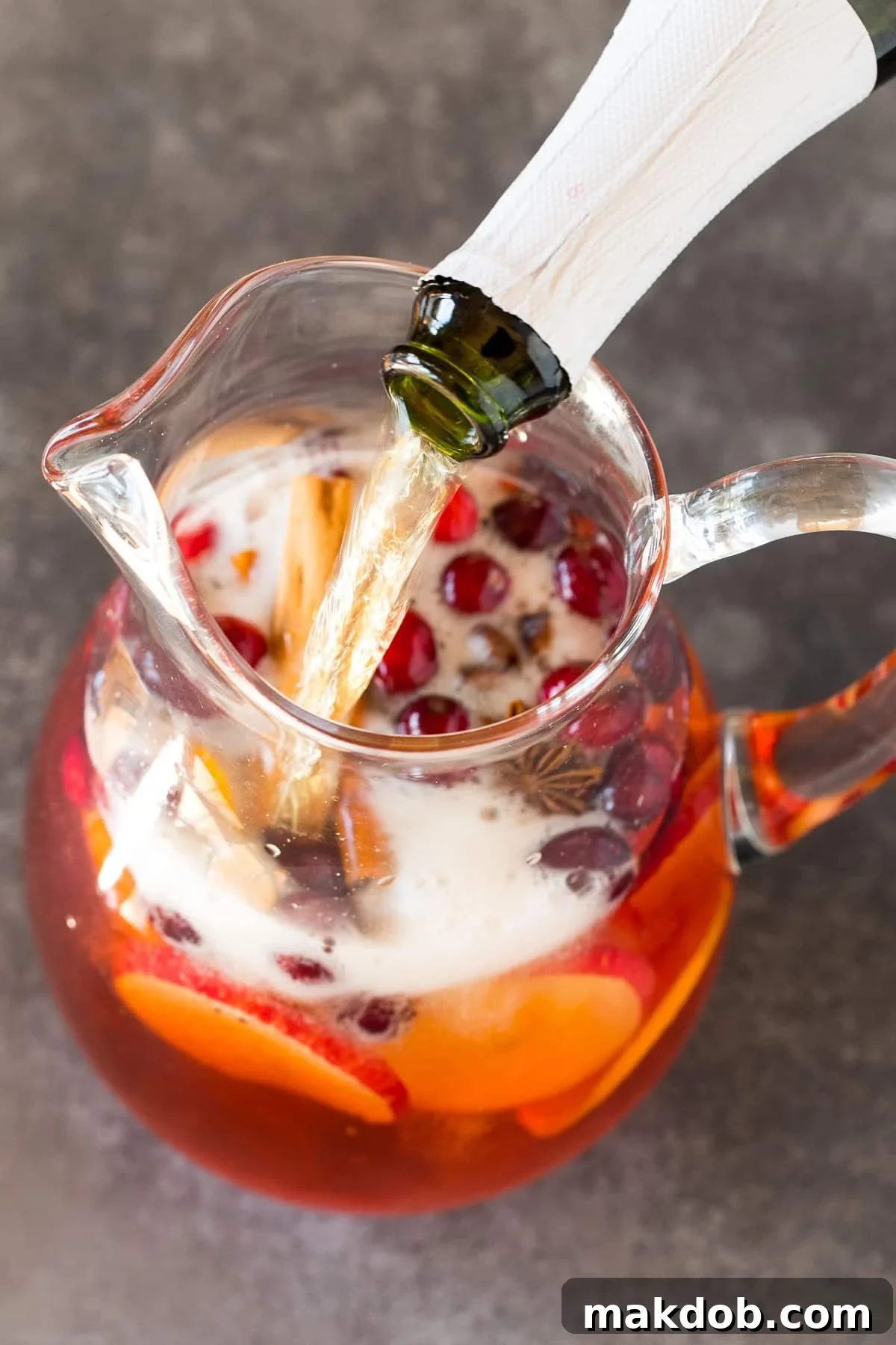 Jolly Christmas Sangria 5 Sparkling cider being poured into a pitcher of sangria.