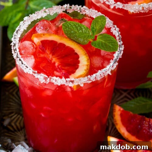 A glass of blood orange margarita with a sugar and salt rim and mint for garnish.