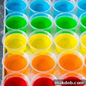 Rows of colorful rainbow-layered Jello shots, perfectly lined up on a sheet pan, ready for a festive party.