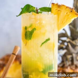 A vibrant Pineapple Mojito in a glass, garnished with fresh mint and a pineapple wedge, capturing its tropical essence.