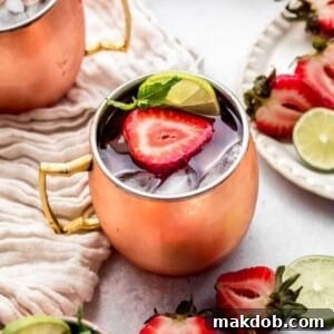 A picture of a gleaming copper mug filled with a Strawberry Moscow Mule, garnished with fresh strawberries and a lime wedge.