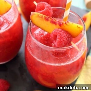A picture of a vibrant Frozen Raspberry Peach Bellini, served in a tall glass, garnished with fresh fruit.