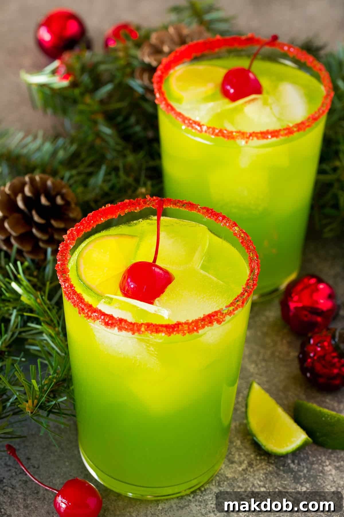 Stolen Holiday Spirit 2 Two cups of Grinch cocktail garnished with cherries and limes.