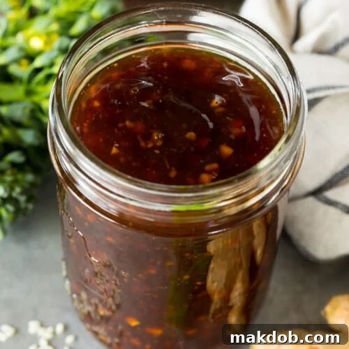 A jar of homemade stir fry sauce surrounded by fresh vegetables.