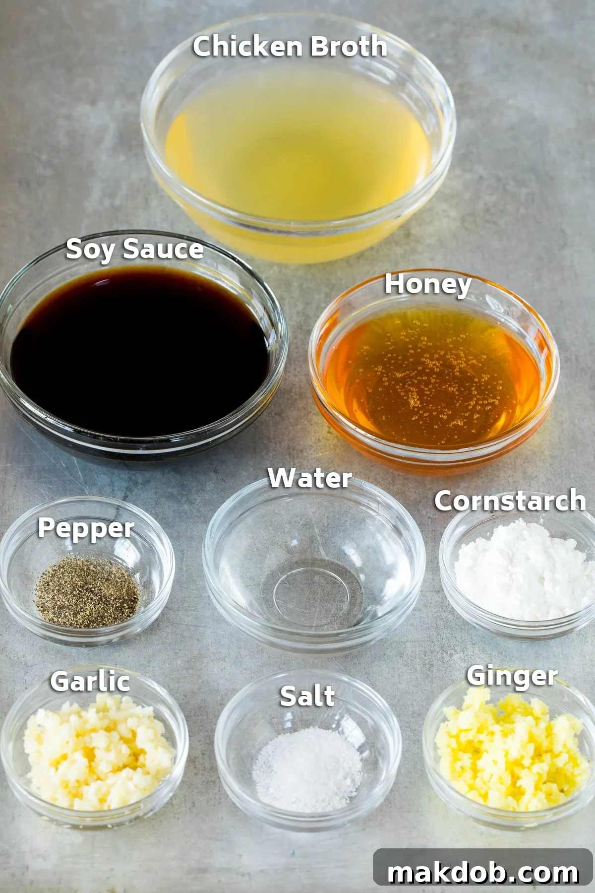 Bowls of essential stir-fry sauce ingredients including chicken broth, soy sauce, fresh ginger, minced garlic, and cornstarch, neatly arranged for preparation.