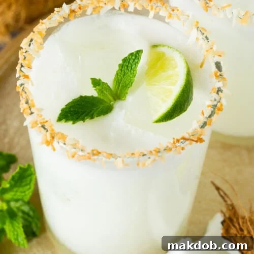 A glass of coconut margarita with a toasted coconut rim and a garnish of mint.