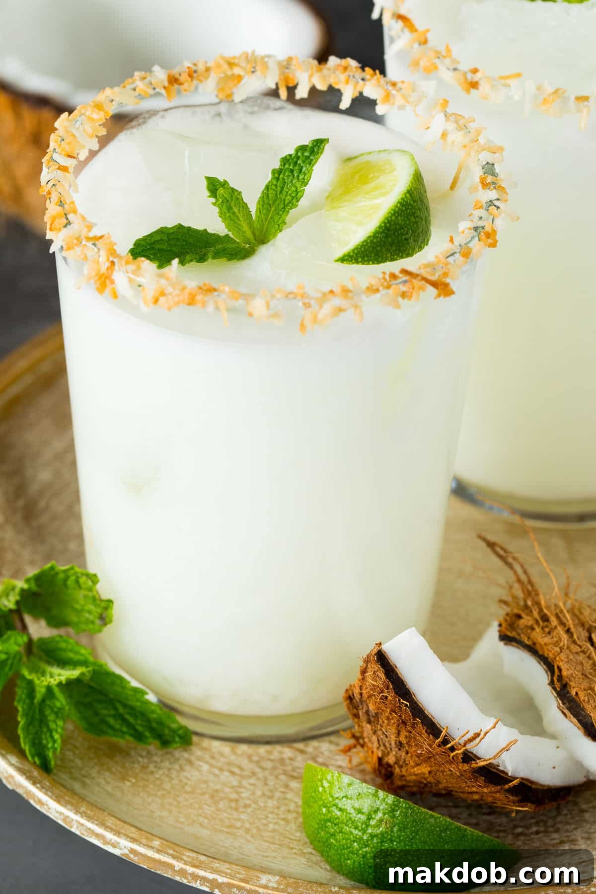 A close-up of a perfectly crafted coconut margarita, garnished with a vibrant lime wedge and a sprig of fresh mint, set against a blurred tropical background.