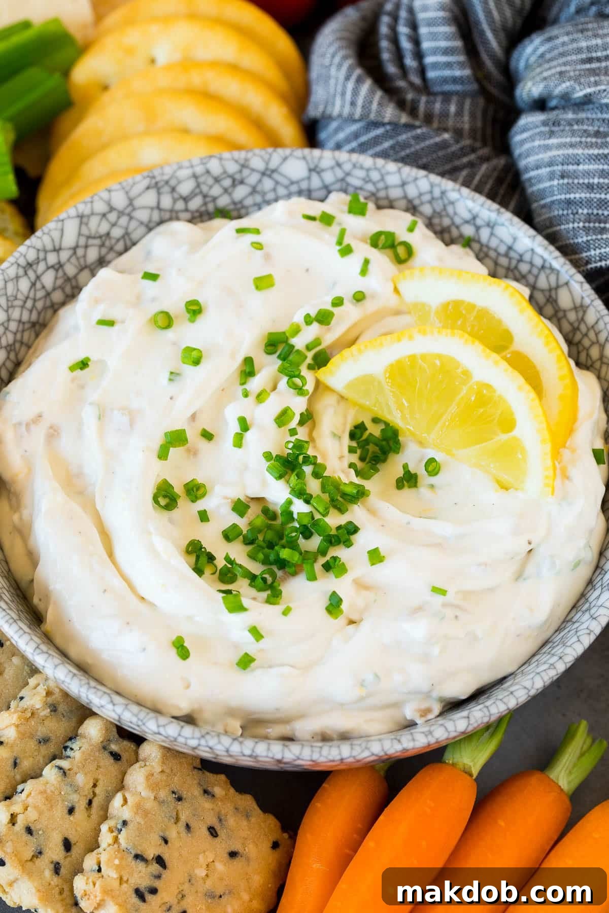 A beautifully presented bowl of creamy clam dip, garnished with fresh chives and delicate lemon slices, ready to be served.