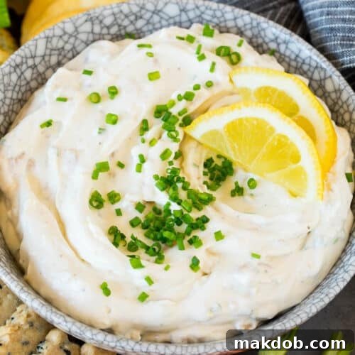 A bowl of clam dip topped with chives and lemon slices, a delicious and inviting appetizer.
