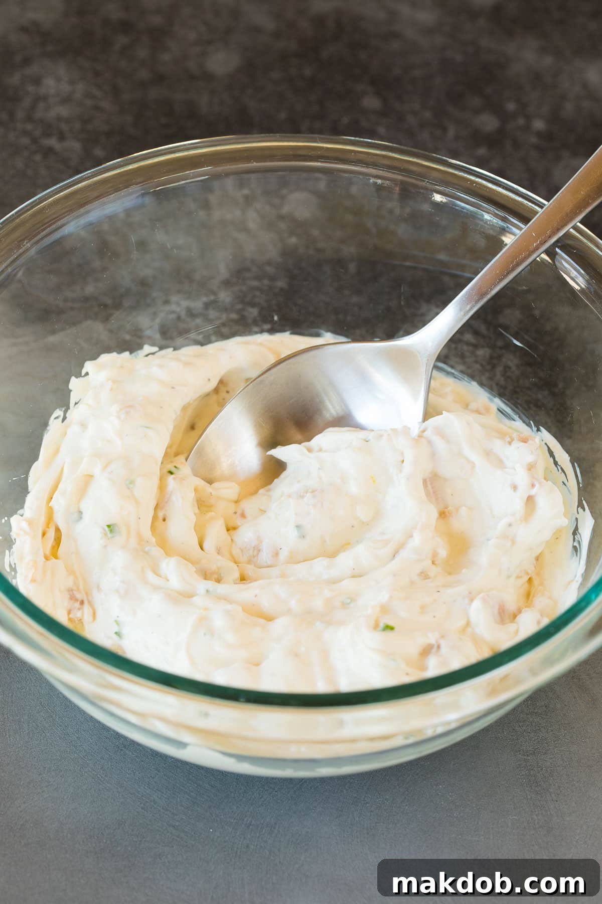 A spoon emerging from a bowl of perfectly creamy, smooth clam dip, ready for chilling and serving.