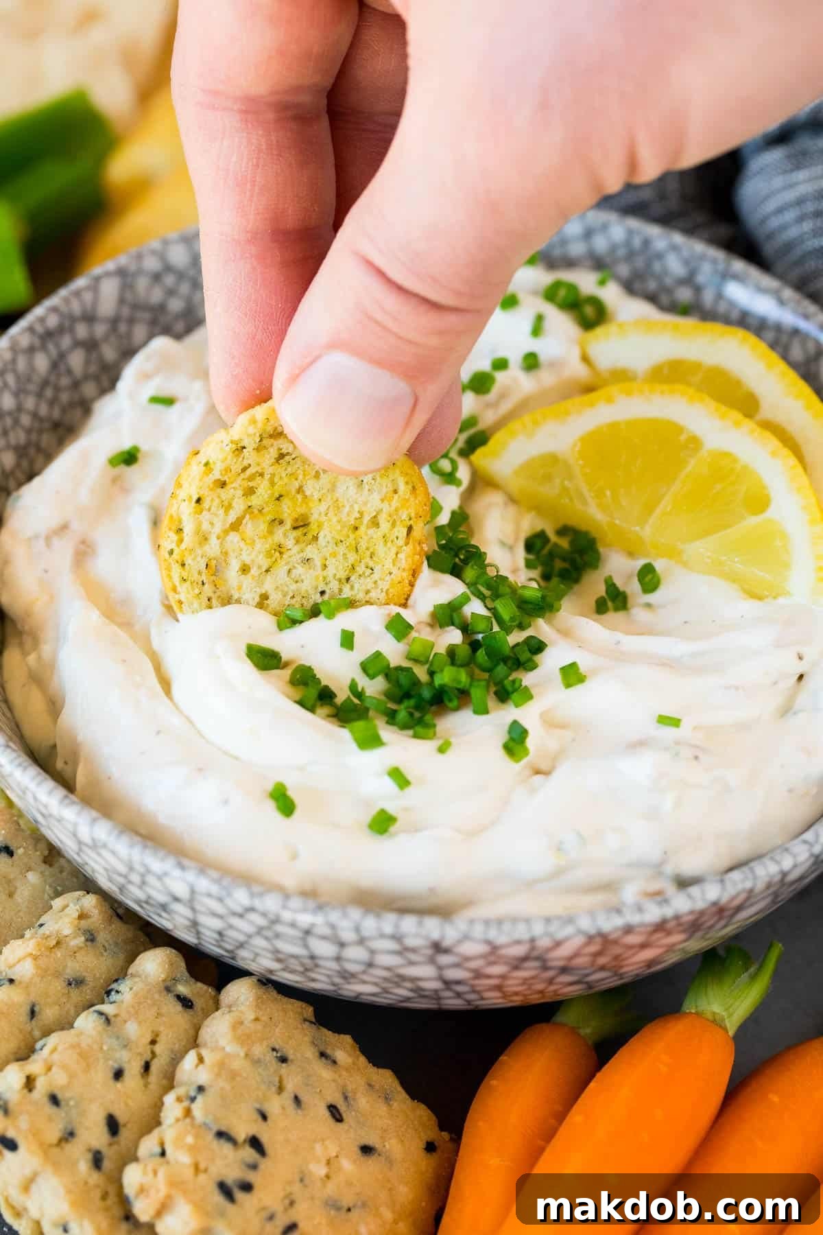 A hand expertly scooping a generous portion of creamy clam dip onto a crisp cracker, emphasizing its irresistible appeal.