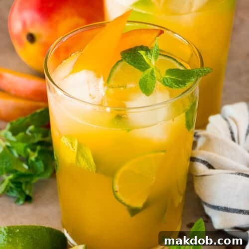 Glasses of mango mojito with garnishes of mint, limes and mango slices.