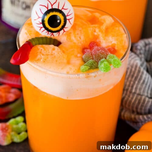 A cup of witches brew topped with a plastic eyeball and gummy candy.