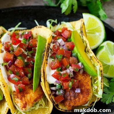 Fish tacos wrapped in corn tortillas with sliced avocado and pico de gallo.