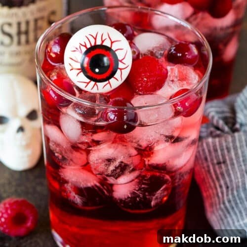 A glass of red Halloween punch with berries and a fake eyeball in it.
