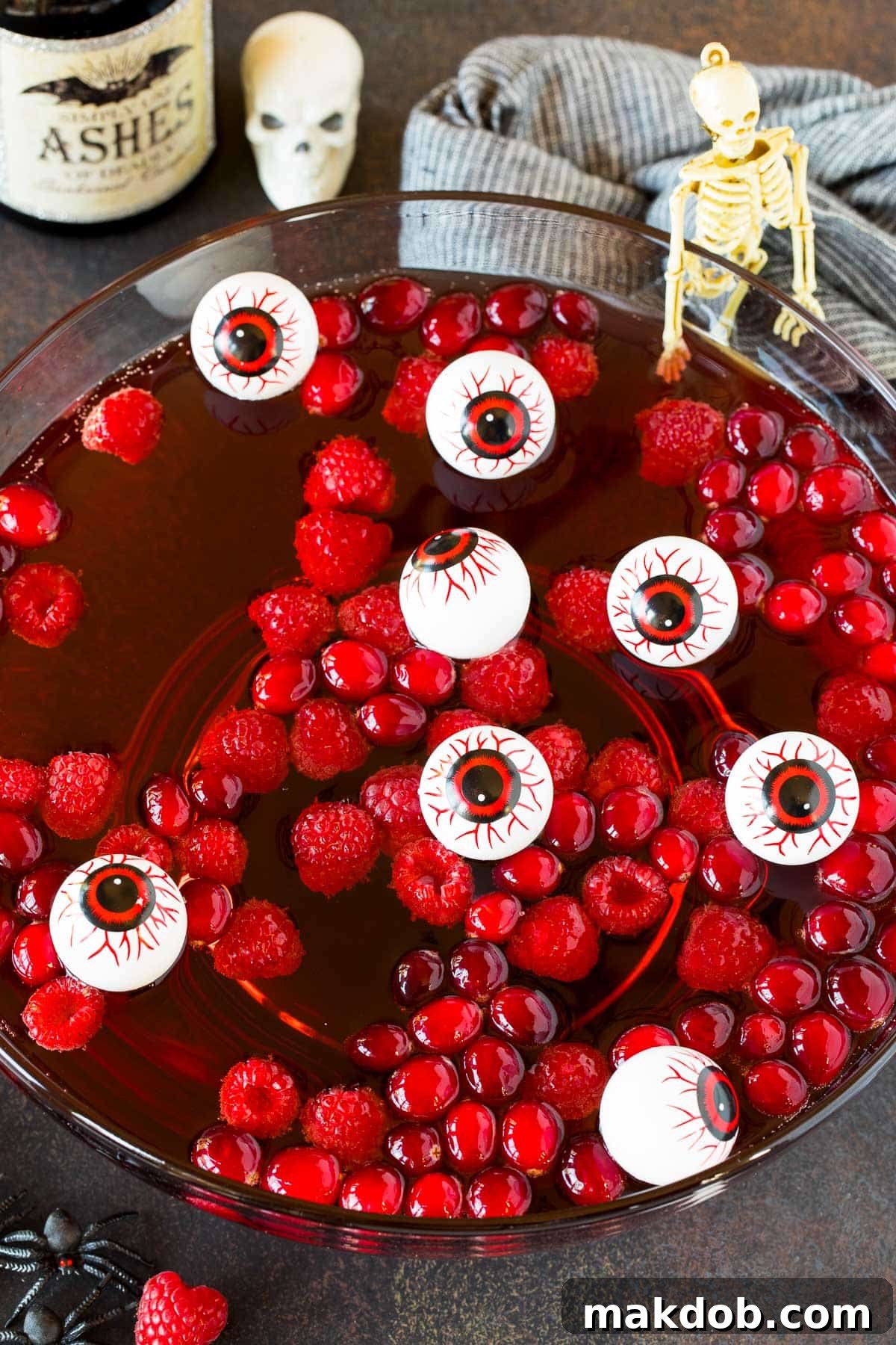 A bowl of Halloween punch with raspberries and cranberries floating in it, garnished with a spooky eyeball.