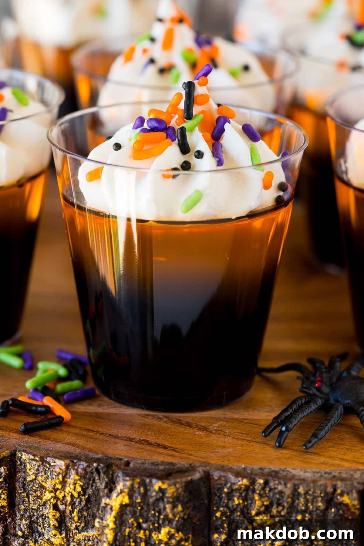 Orange and black layered Halloween Jello shots topped with whipped cream and sprinkles, arranged for a party.