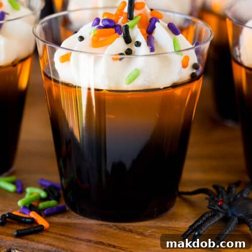 Orange and black layered Halloween Jello shots topped with whipped cream and sprinkles.