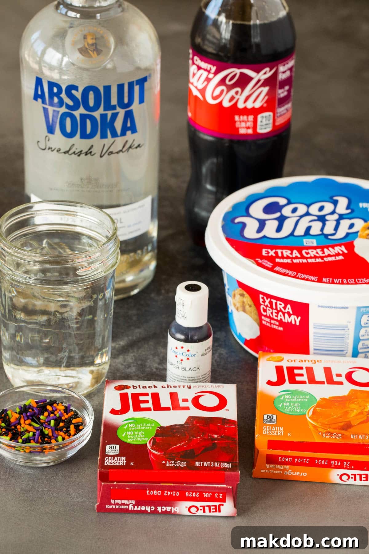 Collection of Halloween Jello shot ingredients including Jello packets, vodka, cherry coke, and whipped topping.