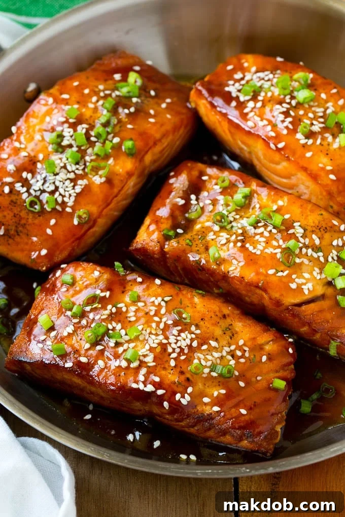 Seared salmon fillets generously coated in glistening homemade teriyaki sauce, garnished with bright green onions and toasted sesame seeds, served on a plate.