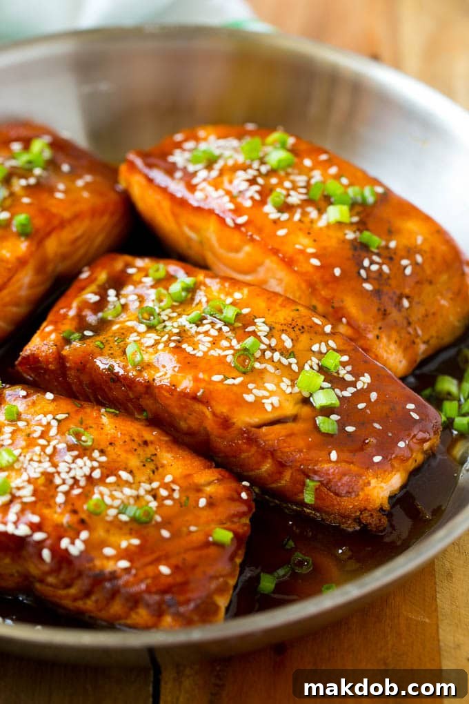 A large pan filled with multiple seared salmon teriyaki fillets, each generously topped with sesame seeds, ready to be served.