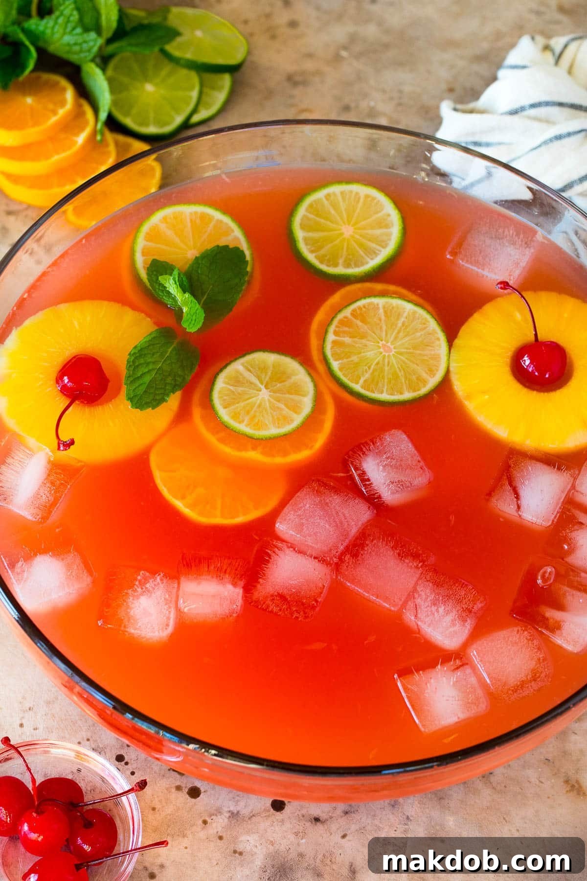 A bowl of vodka punch with citrus slices, pineapple and cherries in it.