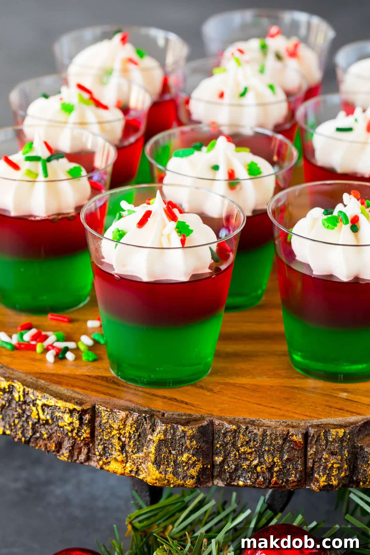 A whole tray of perfectly decorated Christmas Jello shots, each topped with whipped cream and holiday sprinkles, ready to be served at a festive gathering.
