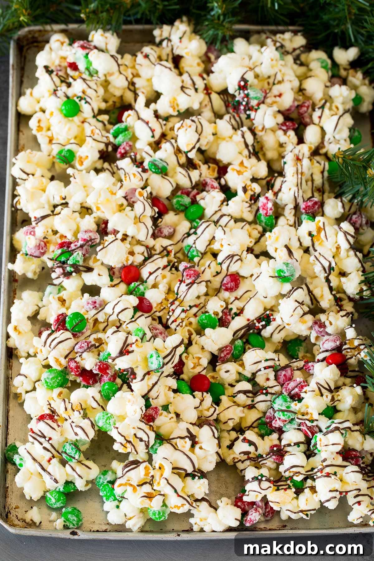 Sparkling Holiday Popcorn 6 An overhead shot of a large batch of Christmas popcorn on a sheet pan, adorned with an abundance of sprinkles and melted chocolate, showcasing its festive appeal.