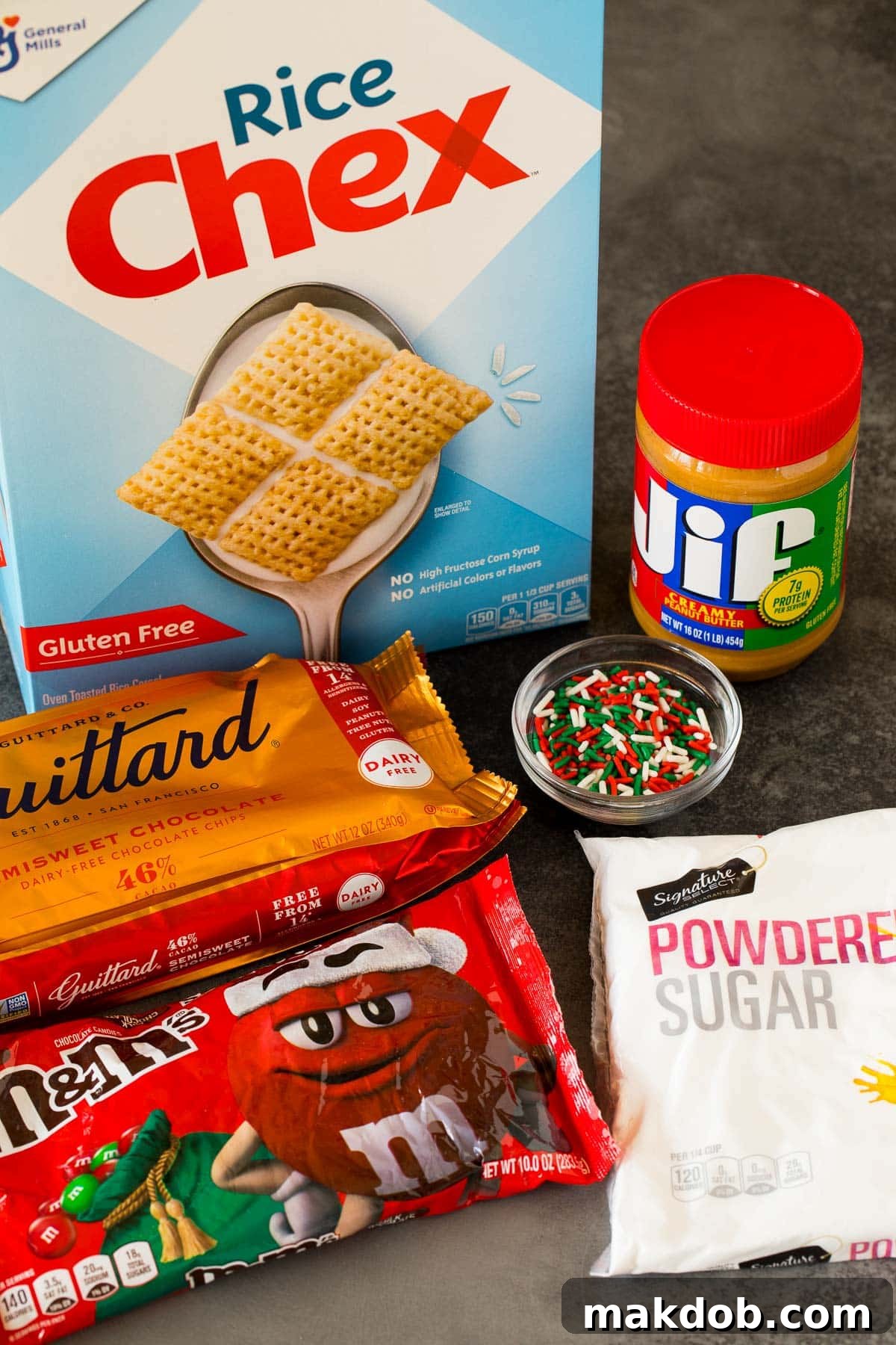 Key ingredients laid out for Christmas puppy chow, including Rice Chex cereal, chocolate chips, creamy peanut butter, and powdered sugar.