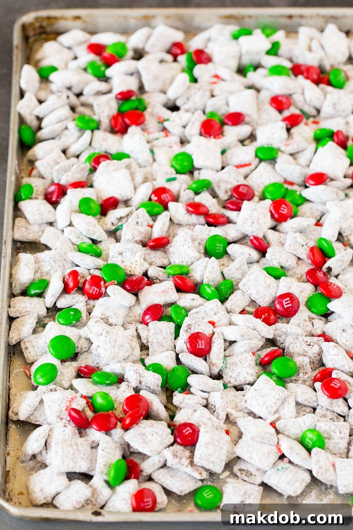 A sheet pan generously filled with festive Christmas puppy chow, showcasing a delightful mix of muddy buddies, red and green M&M's, and holiday sprinkles.