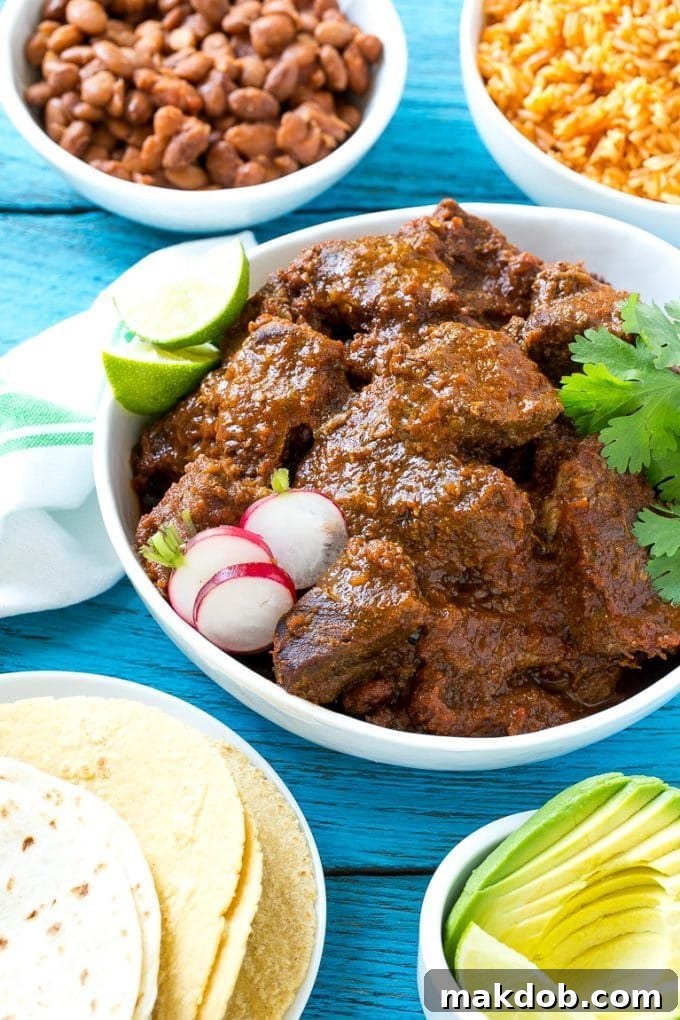 A hearty serving of Mexican stewed beef, known as Chile Colorado, beautifully presented with side bowls of fluffy rice and seasoned pinto beans, inviting a satisfying meal.