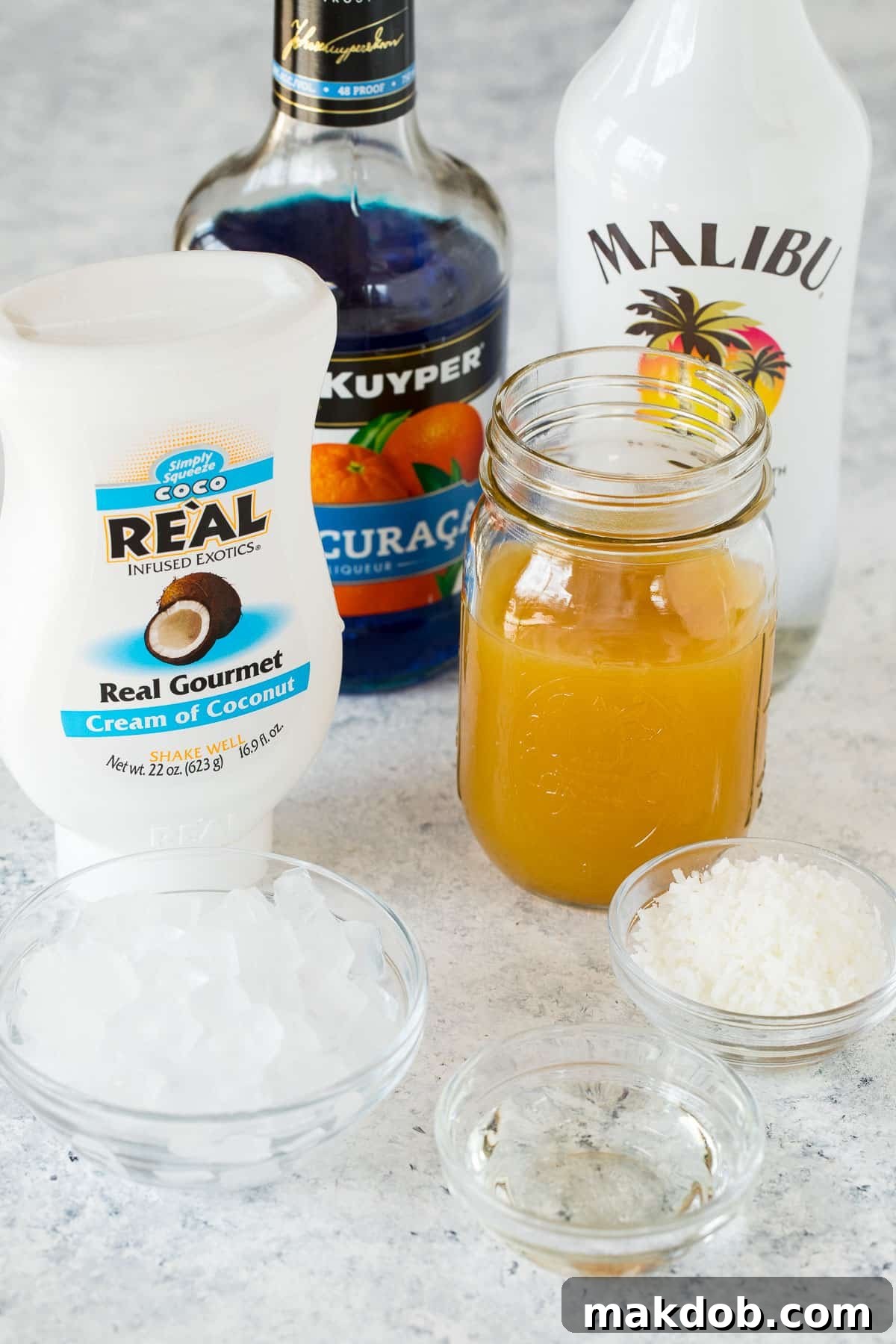 Ingredients for Jack Frost cocktail: pineapple juice, coconut cream, coconut rum, and blue curacao laid out on a table.