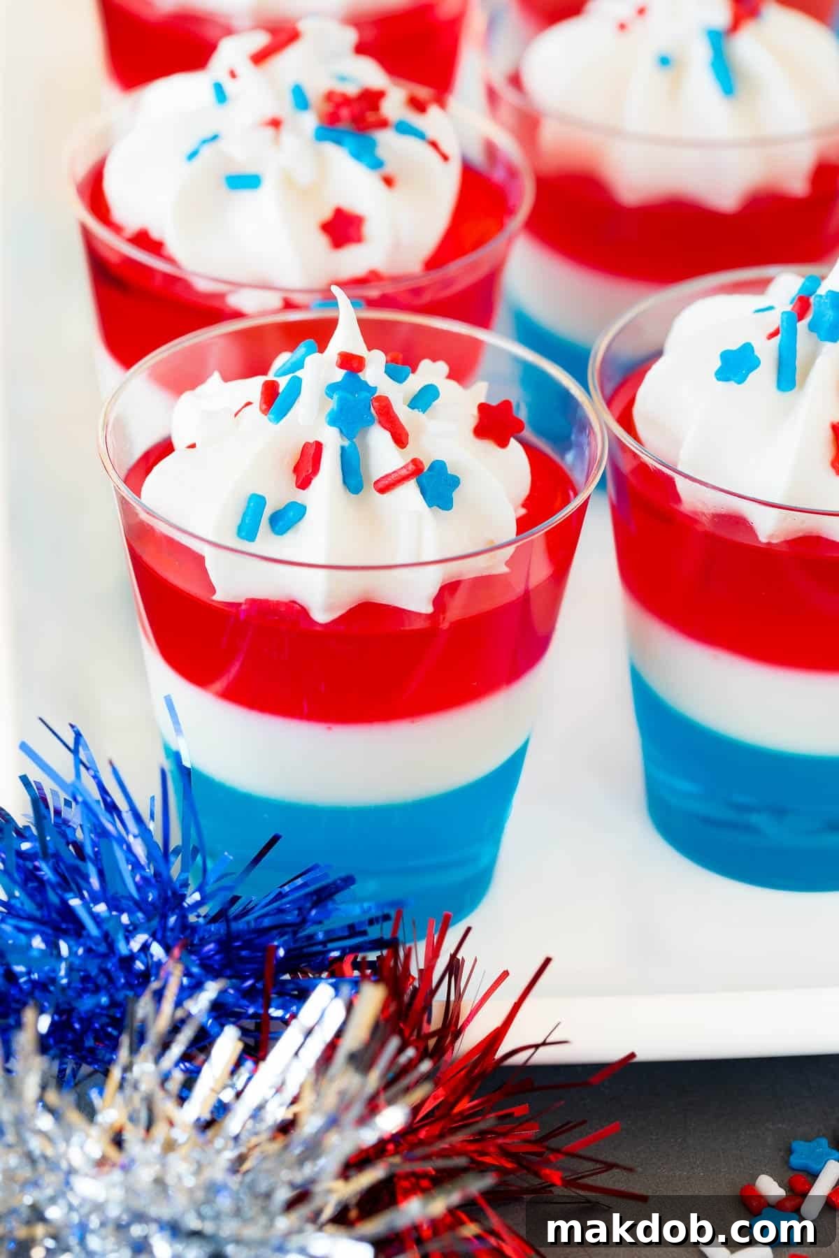 Star-Spangled Jell-O Shooters 2 Red white and blue Jello shots topped with whipped cream and sprinkles, perfect for patriotic celebrations.