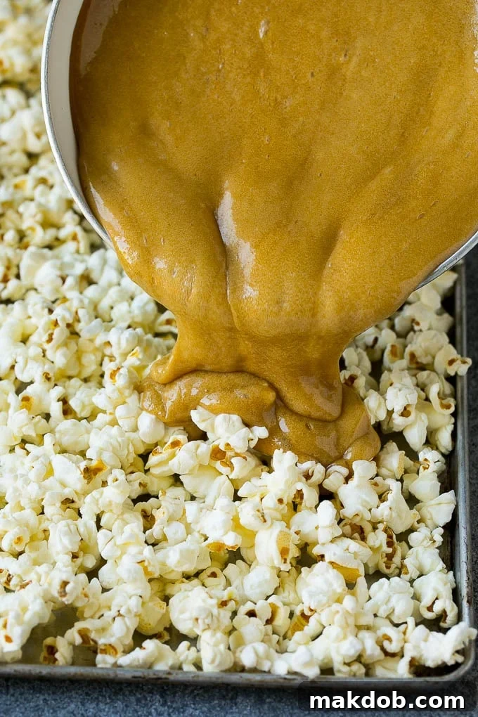 Hot caramel being poured evenly over a large pan of popcorn, ready for coating.