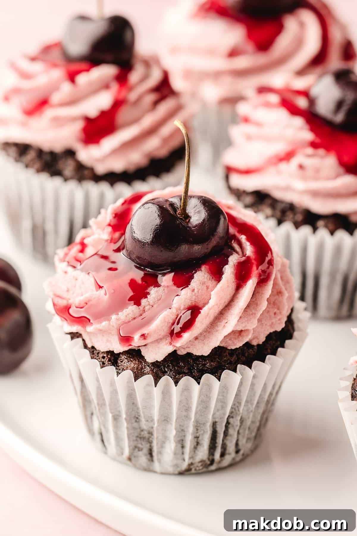 Elegant Black Forest cupcakes adorned with fresh cherries, presented beautifully on a serving plate.