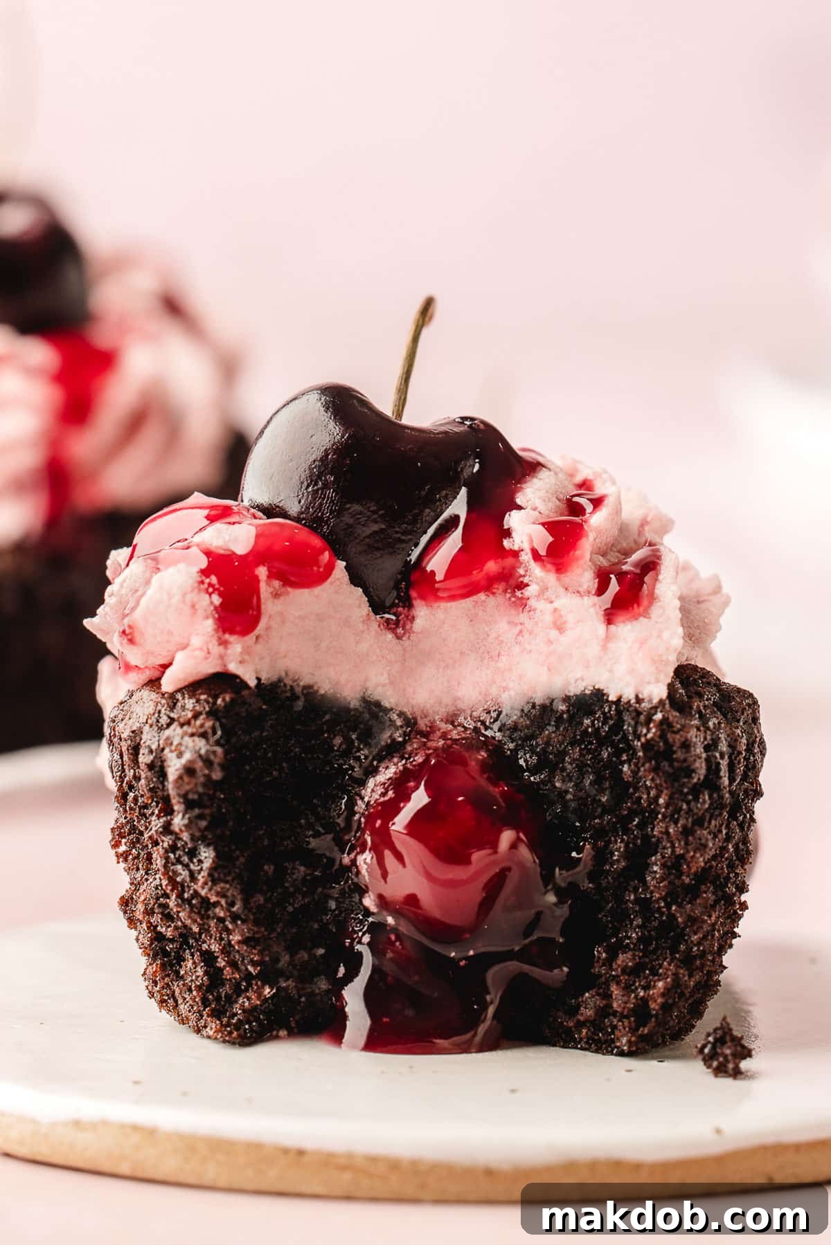 Two enticing Black Forest cupcakes, one cut open to reveal its rich cherry filling inside.