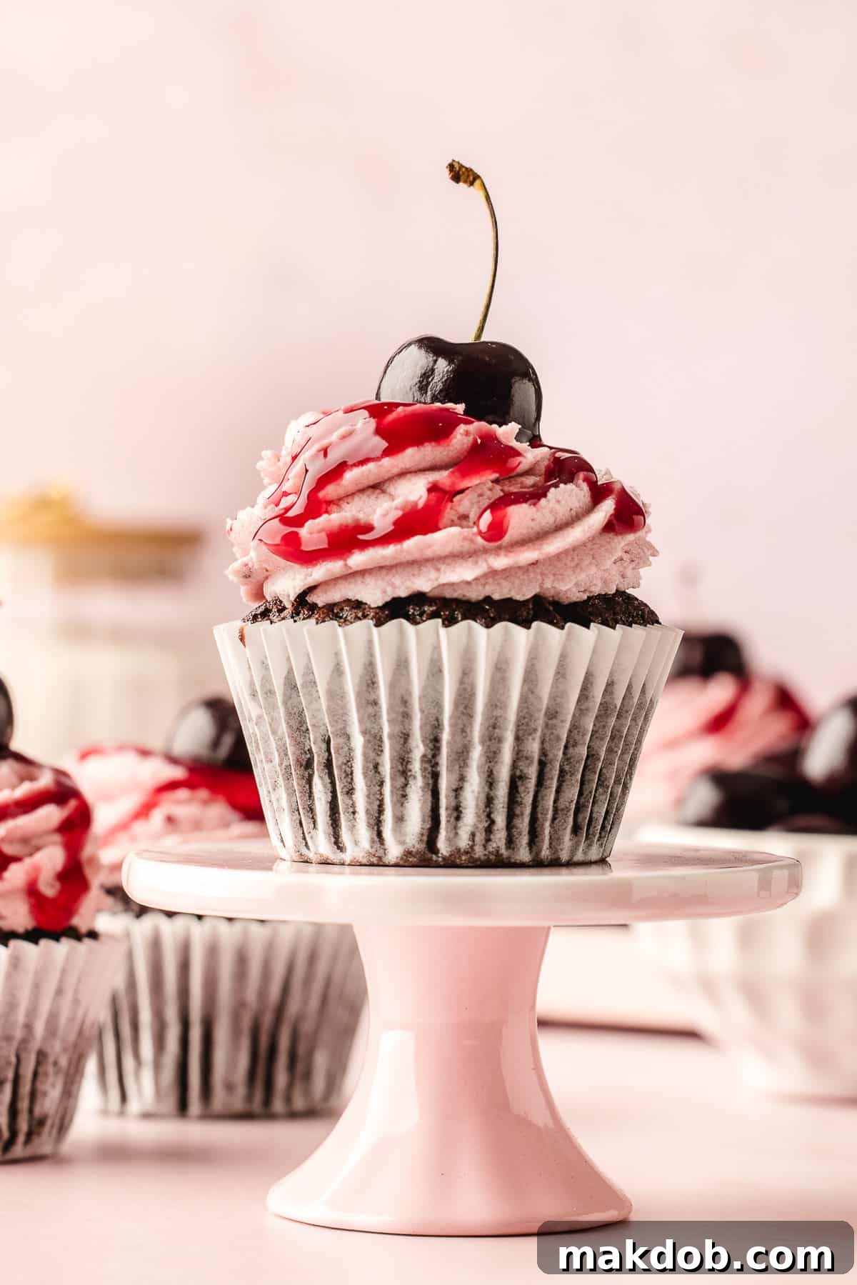 A beautifully decorated chocolate cherry cupcake resting on a elegant pedestal stand.