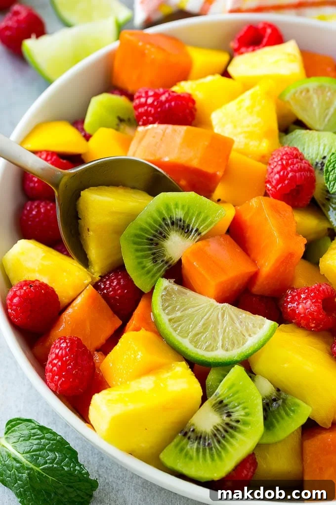Paradise Fruit Bowl 4 A pristine bowl of tropical fruit salad, complete with a serving spoon, showcasing the luscious blend of mango, pineapple, papaya, kiwi, and raspberries.