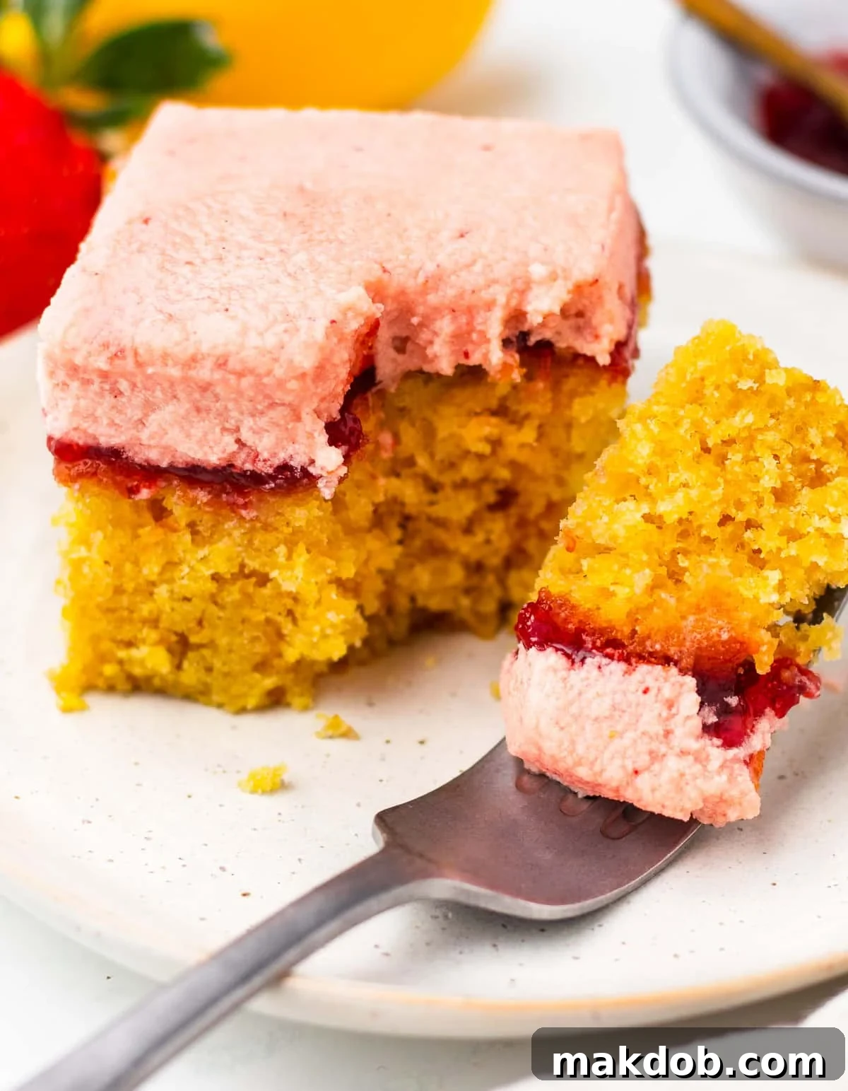 Sunshine Strawberry Lemon Cake 6 A delectable slice of strawberry lemon cake with a fork gently taking a piece, highlighting its soft texture and flavorful layers.