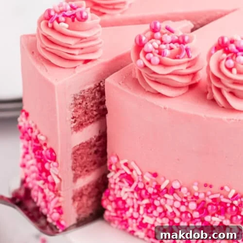 A vibrant Pink Velvet Cake with a slice removed, adorned with festive sprinkles and creamy Swiss meringue buttercream.
