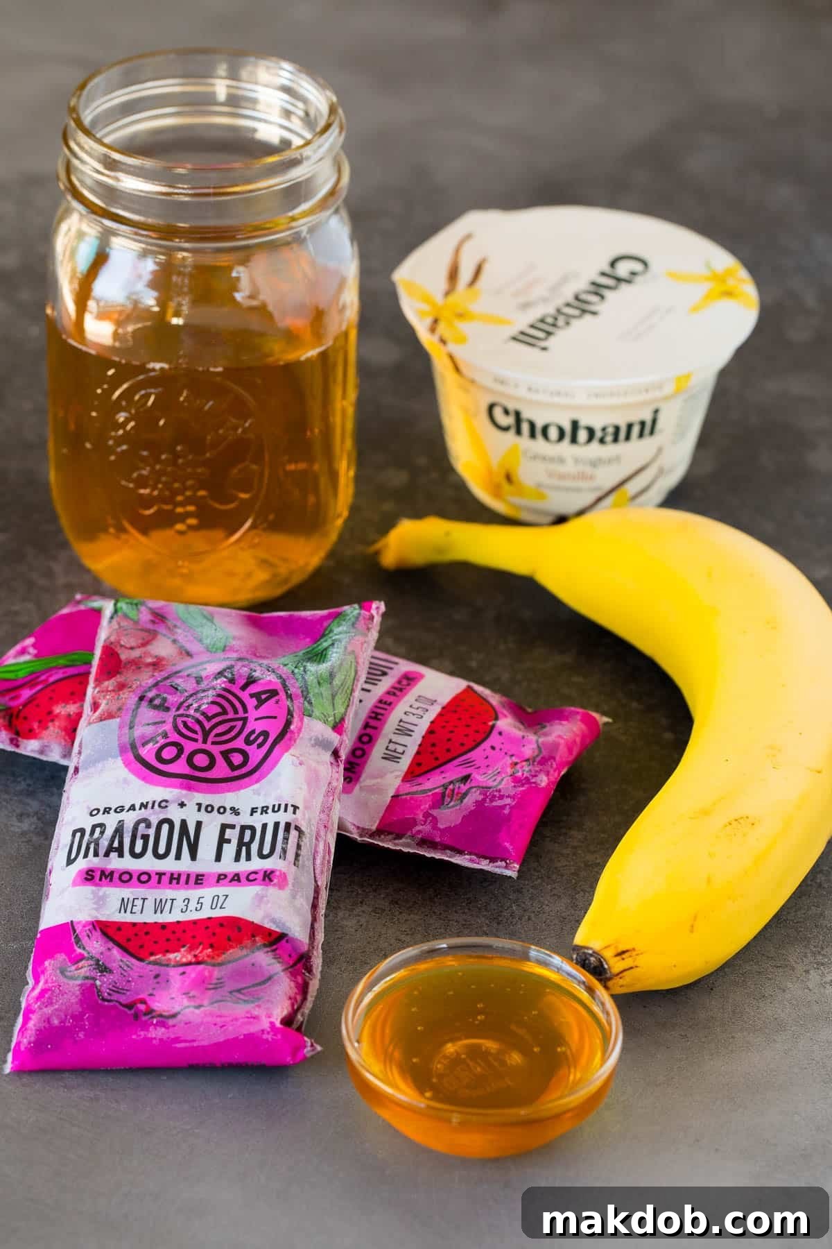 Honey, yogurt, banana, frozen fruit and apple juice laid out as ingredients for a dragon fruit smoothie.