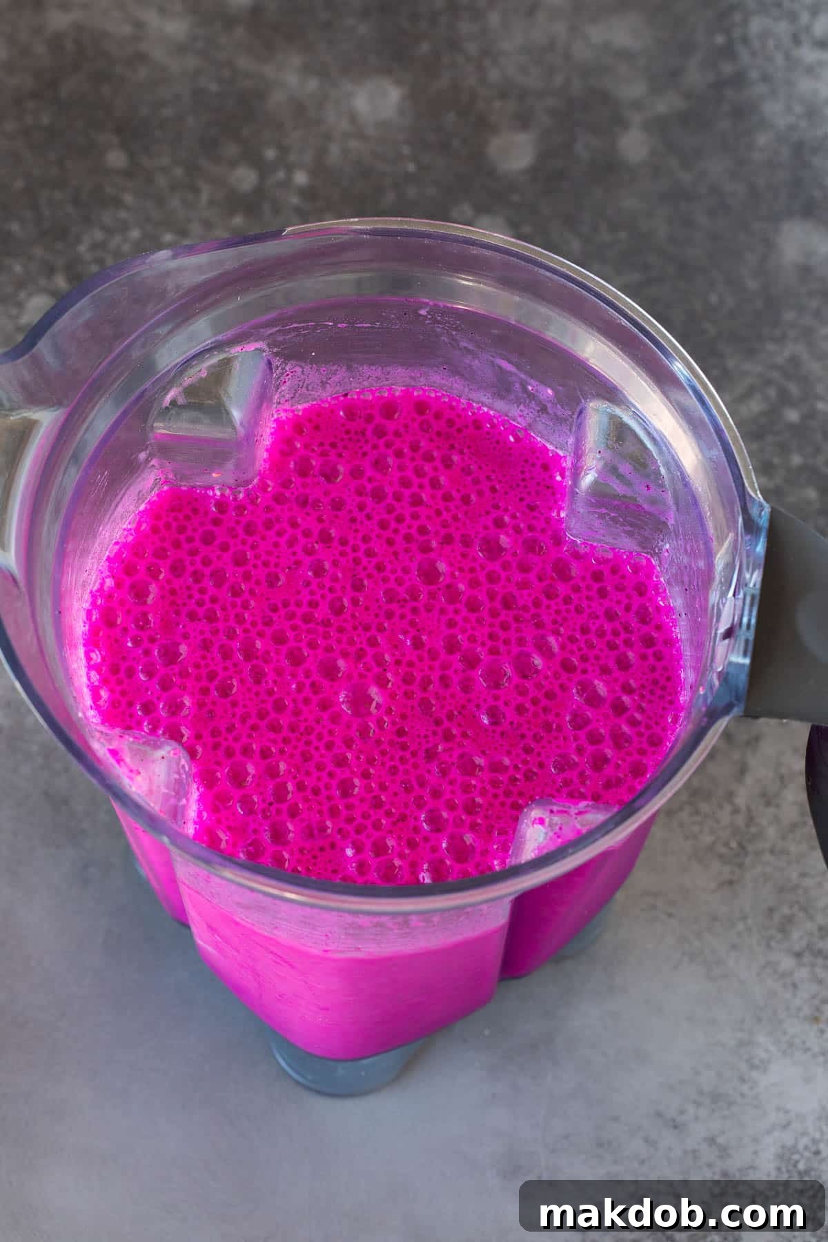 A vibrant pink dragon fruit smoothie being mixed in a blender.