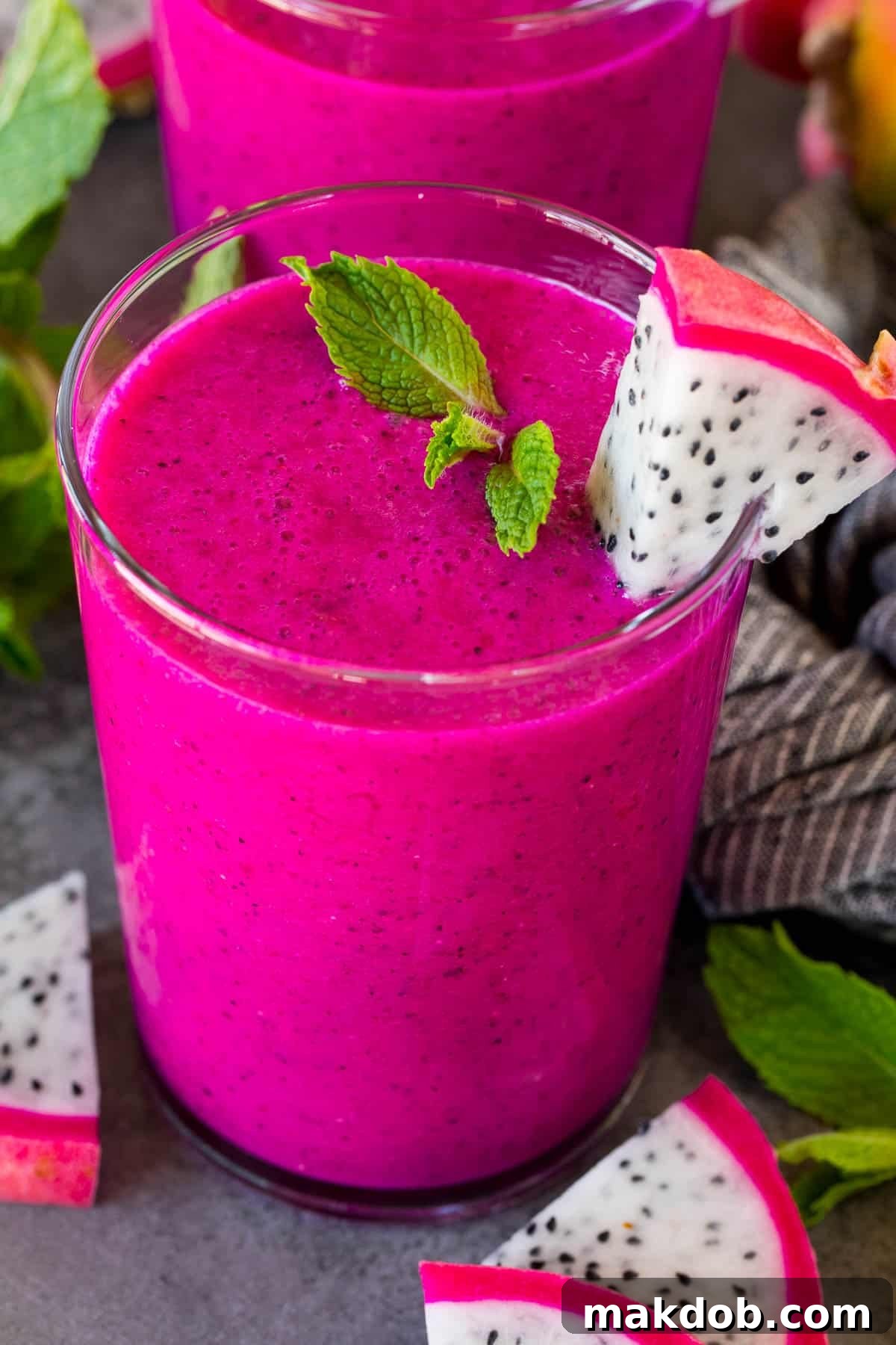 A glass of vibrant pink dragon fruit smoothie garnished with a mint sprig and a slice of fresh dragon fruit.