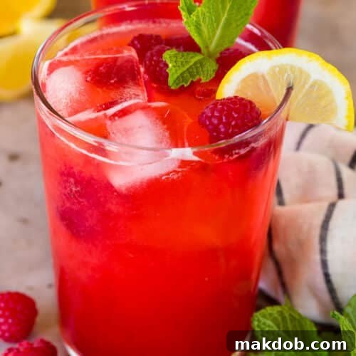 A glass of raspberry lemonade garnished with berries and a lemon slice.